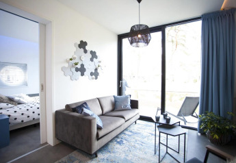 Stylish living room at Modus L lodge, De Zanding, Netherlands, with sofa, large window, and bedroom view.