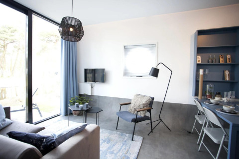 Sala moderna en la cabaña Modus L de De Zanding, Países Bajos, con ventanas grandes y decoración acogedora.