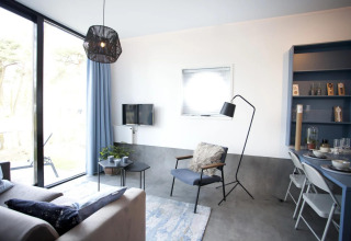 Sala moderna en la cabaña Modus L de De Zanding, Países Bajos, con ventanas grandes y decoración acogedora.