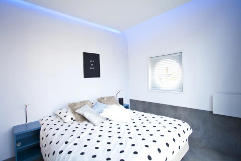 Dormitorio moderno en Modus L, De Zanding, Países Bajos con ropa de cama de lunares y luz azul ambiental.