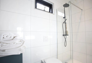 Salle de bain moderne au Modus L, De Zanding, Pays-Bas, avec douche à effet pluie, paroi vitrée et serviettes.
