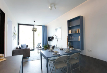 Modern living and dining area of Modus L lodge at De Zanding, Netherlands, with blue decor and sunlight.