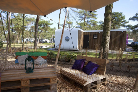 Coin salon extérieur avec bancs en palettes et lanterne à la lodge Modus L, De Zanding, Pays-Bas, en forêt.
