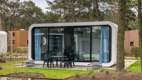 Modern Modus L lodge at De Zanding in the Netherlands, featuring glass façade, patio seating, and pine trees.