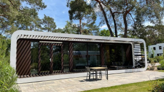 Moderna cabaña llamada Mode Sauna en De Zanding, Países Bajos, rodeada de árboles y jardín soleado.