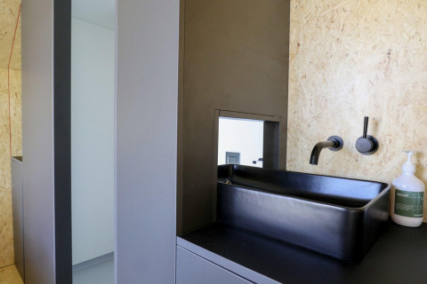 Baño moderno con lavabo cuadrado negro, grifo de pared y dispensador de jabón en De Zanding, Países Bajos.