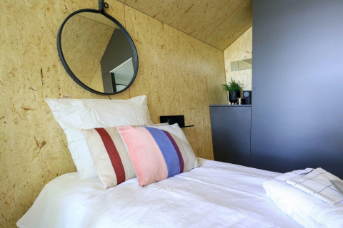 Moderne enkelt seng med farverige puder, rundt spejl og minimalistisk indretning på Solo retreat i De Zanding, Holland.