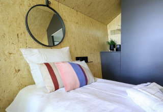 Cama individual moderna, cojines coloridos y espejo redondo en Solo retreat de De Zanding, Países Bajos.