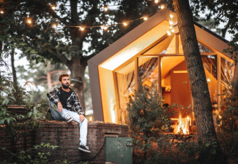 Man zit buiten bij een verlichte lodge omringd door bomen bij Solo retreat op De Zanding in Nederland.