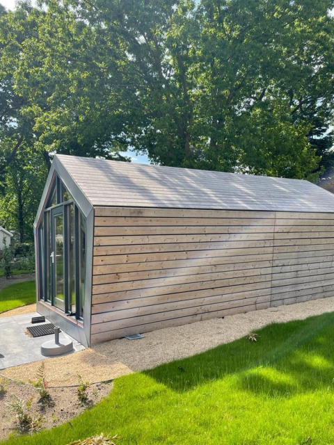 Moderna cabaña de madera en Solo Retreat, De Zanding en los Países Bajos, rodeada de césped y árboles.