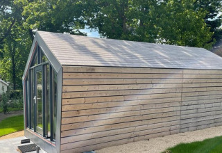 Moderne houten lodge bij Solo Retreat, De Zanding in Nederland, omgeven door gras en hoge bomen.