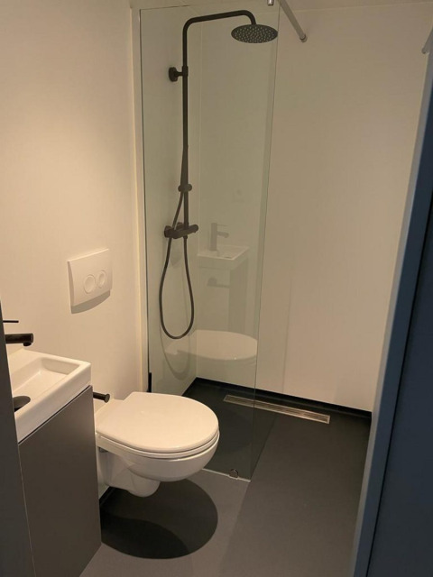 Baño moderno en Solo Retreat, De Zanding, Países Bajos, con inodoro, pequeño lavabo y ducha abierta.