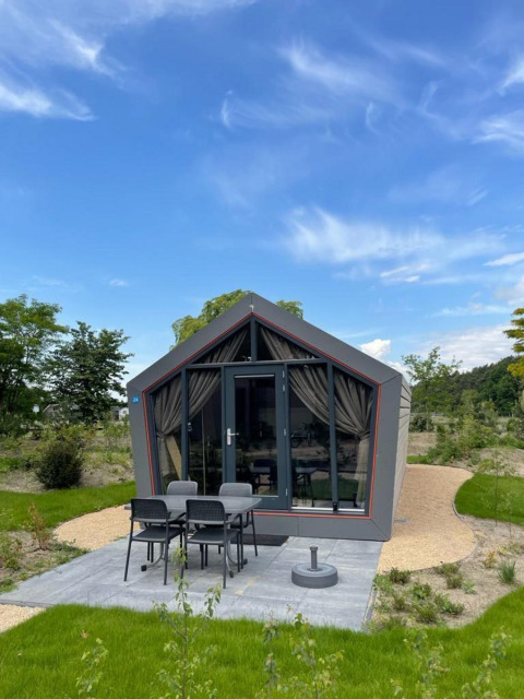 Solo Retreat lodge aan De Zanding in Nederland, modern huisje met terras, vier stoelen en groene tuin.