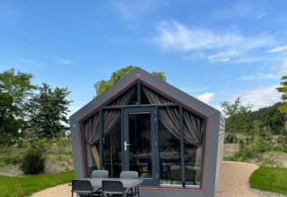 Solo Retreat lodge aan De Zanding in Nederland, modern huisje met terras, vier stoelen en groene tuin.