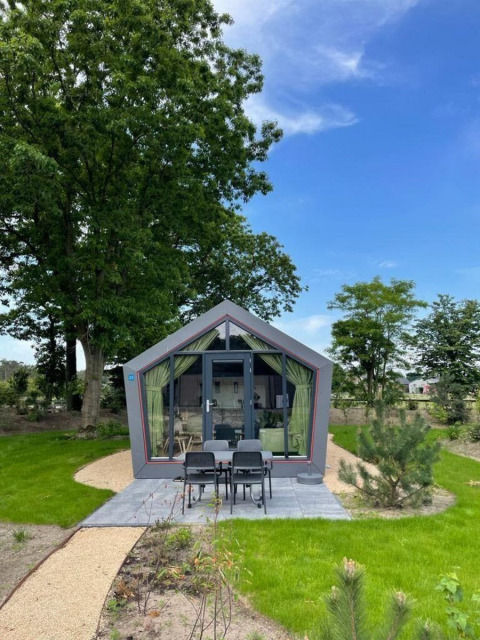 Moderne Solo Retreat lodge bij De Zanding, Nederland, met terras, tuin, bomen en blauwe lucht eromheen.