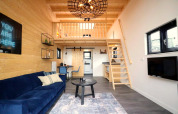 Intérieur moderne de tiny house avec mezzanine, canapé bleu, murs en bois et escalier gain de place.