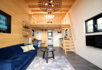 Moderne tiny house interiør med hems, blå sofa, trævægge og pladsbesparende trappe i Holland.