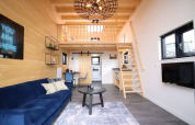 Modern tiny house interieur met slaapzolder, blauwe bank, houten wanden en ruimtebesparende trap.