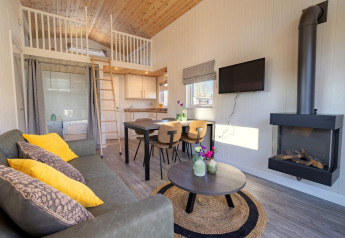 Alloggio glamping moderno con soppalco, soffitto in legno, divano accogliente, tavolo e camino.