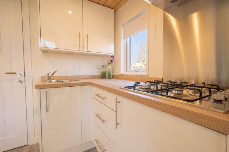 Cocina moderna y compacta en alojamiento glamping, equipada con encimera de gas, fregadero y ventana.