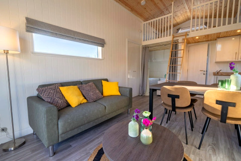 Modernes Glamping-Unterkunft mit Sofa, Esstisch, Hochbett und stilvollem Interieur in Naturtönen.