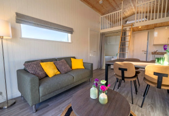 Alloggio glamping moderno con divano, tavolo da pranzo, soppalco e arredo elegante in toni naturali.