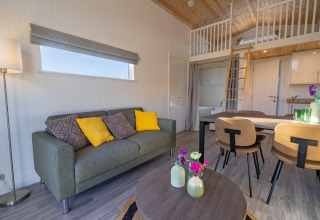 Alojamiento glamping moderno con sofá, mesa de comedor, altillo y decoración elegante en tonos naturales.
