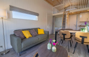 Moderne glamping indkvartering med sofa, spisebord, hems og stilfuld indretning i naturlige farver.