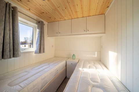 Bright glamping accommodation bedroom with two twin beds, a window, wood ceiling, and gray curtains.