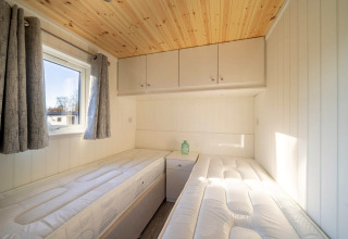 Lyst værelse i et glamping-ophold med to enkeltsenge, et vindue, grå gardiner og trægulv.