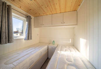 Stanza luminosa in alloggio glamping con due letti singoli, finestra, tendaggi grigi e soffitto in legno.