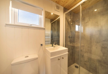 Bagno moderno con doccia in vetro, lavabo bianco e WC in una sistemazione glamping dal soffitto in legno.