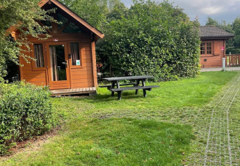 Zona verde con mesa de picnic y cabañas de madera en Urban-Gardens Ieper, Basic log cabin, Bélgica.
