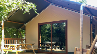 Tienda de glamping familiar en Urban-Gardens Ieper, Bélgica, con terraza, banco de picnic y vistas verdes.