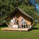 To personer nyder en drink foran en Glampingtent XS i Urban-Gardens Ieper, Belgien, omgivet af natur.
