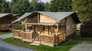 Tenda safari alla Ranger Lodge con veranda in legno, immersa tra alberi e prato in un ambiente tranquillo.
