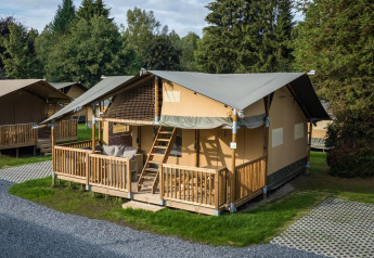 Tenda safari alla Ranger Lodge con veranda in legno, immersa tra alberi e prato in un ambiente tranquillo.