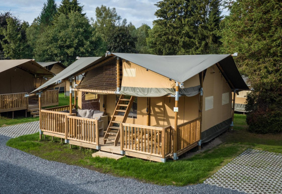 Safaritent in Ranger Lodge met houten terras, omringd door bomen en gras in een rustige, groene omgeving.