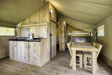 Interior de una tienda safari con muebles de madera, cocina, mesa de comedor y literas en Comet 27 Lodges.