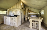 Interior de una tienda safari con muebles de madera, cocina, mesa de comedor y literas en Comet 27 Lodges.