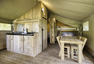 Interior de una tienda safari con muebles de madera, cocina, mesa de comedor y literas en Comet 27 Lodges.