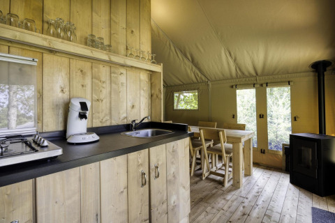 Innenraum eines Safarizelts mit Holzküche und Esstisch in Comet 27 Lodges, Arden Parks, Signy l'Abbaye, Frankreich.