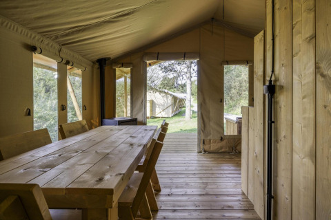 Interior de una tienda tipo safari con mesa y sillas de madera y vista al exterior natural y verde.