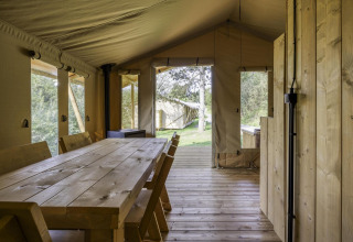 Interior de una tienda tipo safari con mesa y sillas de madera y vista al exterior natural y verde.