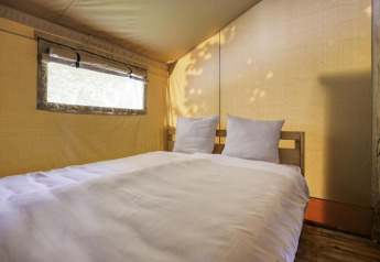 Interieur van een safaritent met tweepersoonsbed bij Comet 27 Lodges in Arden Parks, Signy l'Abbaye, Frankrijk.