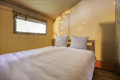 Innenraumaufnahme eines Safari-Zeltes mit gemütlichem Doppelbett bei Comet 27 Lodges in Arden Parks, Frankreich.