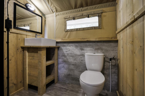 Baño en una tienda safari con paredes de madera, inodoro, lavabo y espejo en Comet 27 Lodges, Francia.