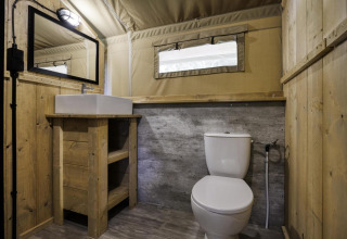 Baño en una tienda safari con paredes de madera, inodoro, lavabo y espejo en Comet 27 Lodges, Francia.