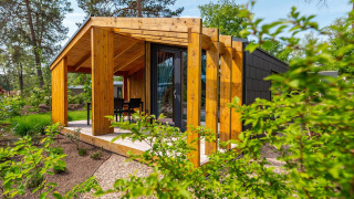Panorama Cottage Tiny House mit moderner Holzveranda, eingebettet in grüner Natur und Bäumen.