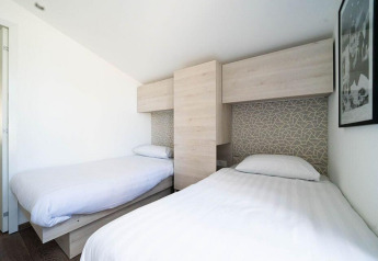 Alloggio glamping moderno con due letti singoli, mobili in legno chiaro e arte astratta sulle pareti.